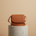 Cognac leather crossbody bag on a stone pedestal